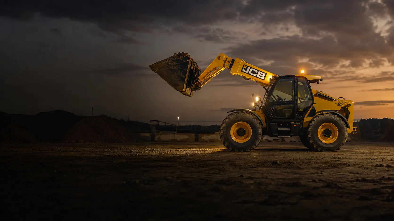 Телескопический погрузчик JCB с навесным ковшом на сумеречной строительной площадке, стрела приподнята